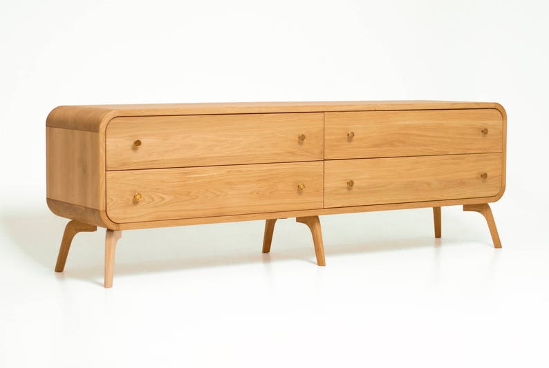 May include: A light wood dresser with four drawers and rounded edges. The dresser has four legs and brass knobs.