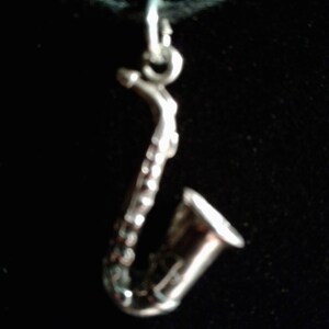 May include: A silver saxophone charm necklace. The charm is detailed and has a realistic design.