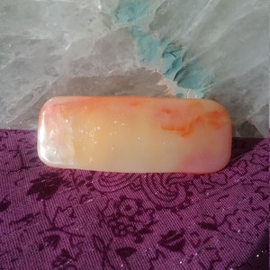 May include: A rectangular, translucent, orange and white agate stone with a smooth, polished surface.