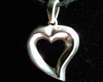 May include: A silver heart-shaped pendant with an open center, hanging from a black cord.