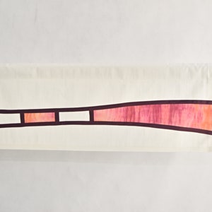 Op de afbeelding: Een witte stoffen banner met een gebogen, bordeauxrode en roze streep met drie witte vierkanten. De banner hangt aan een metalen stang.