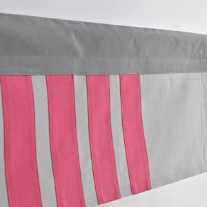 Peut inclure: Une cantonnière à rayures grises et roses avec une bordure supérieure grise. La cantonnière est suspendue à une tringle en métal.