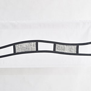 Peut inclure: Une cantonnière blanche avec un motif de ligne ondulée noire comportant une série de découpes rectangulaires avec un recouvrement de tissu texturé.