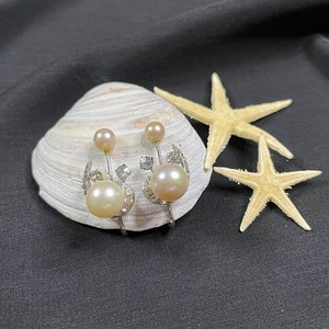 May include: A pair of pearl and rhinestone earrings with a delicate floral design. The earrings are displayed on a seashell with two starfish.