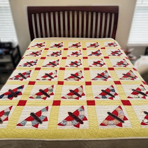 May include: A yellow and red quilt with a pattern of flying birds. The quilt is made of patchwork fabric and is displayed on a bed.