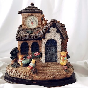 May include: A ceramic clock shaped like a house with a brown roof, white walls, and a clock face with black hands. There are four teddy bears on the front of the house, two sitting on the steps and two standing on the roof.