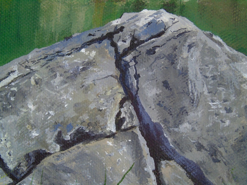 May include: Close-up of a painted rock formation. The rock is primarily gray with lighter and darker shades, and a prominent dark crack runs through it. The background features green and tan hues, suggesting a natural landscape.
