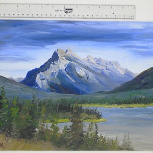 May include: A painting of a mountain range with a lake in the foreground. The mountains are painted in shades of blue and gray, and the lake is a light blue. The sky is a light blue with some white clouds.