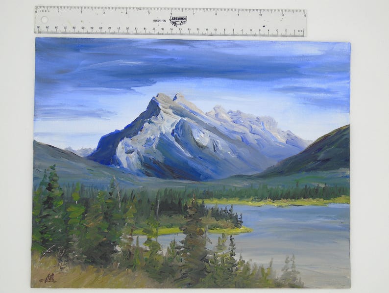 May include: A painting of a mountain range with a lake in the foreground. The mountains are painted in shades of blue and gray, and the lake is a light blue. The sky is a light blue with some white clouds.