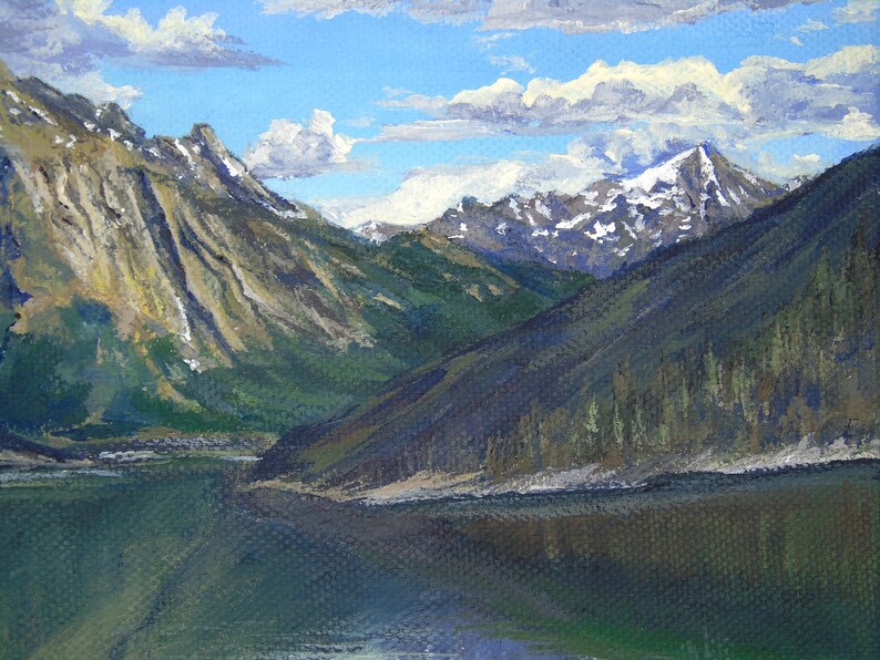May include: Oil painting of a mountain landscape with a lake. The artwork depicts snow-capped peaks, green hills, and a calm lake reflecting the sky. The sky is blue with fluffy white clouds.