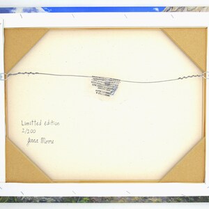 May include: Back of a framed canvas print with a landscape image. The canvas is stretched over a wooden frame, secured with staples. The text "Limited edition 2/200 Jenna Moore" is handwritten on the canvas.