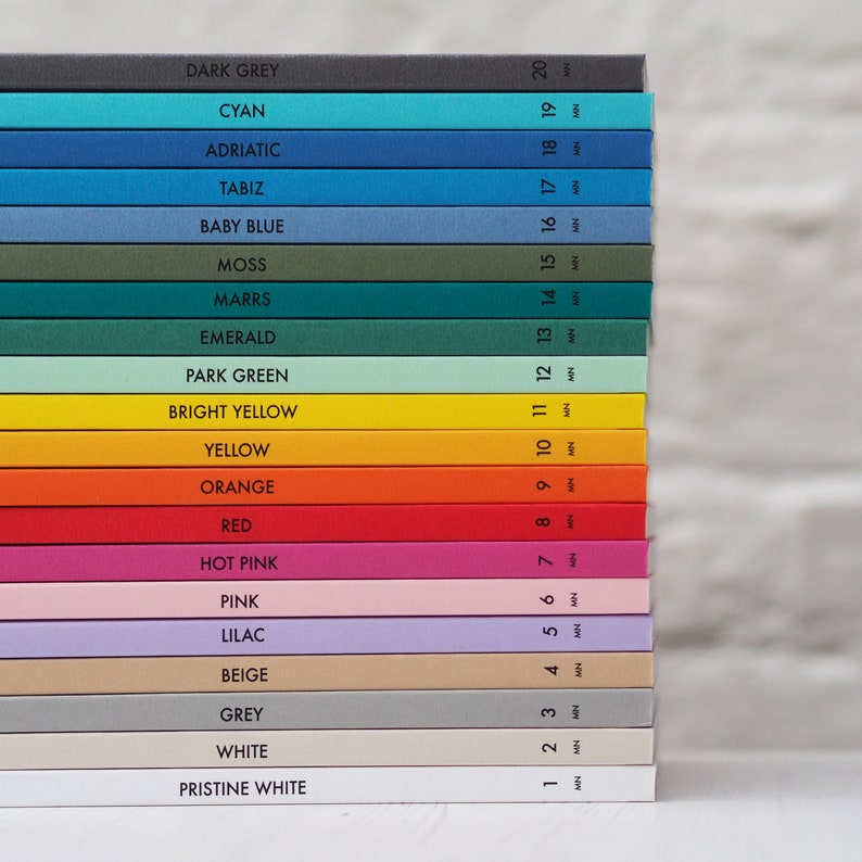 May include: A stack of colorful notebooks with the names of the colors printed on the spine. Colors include dark grey, cyan, adriatic, tabiz, baby blue, moss, marrs, emerald, park green, bright yellow, yellow, orange, red, hot pink, pink, lilac, beige, grey, white, and pristine white.