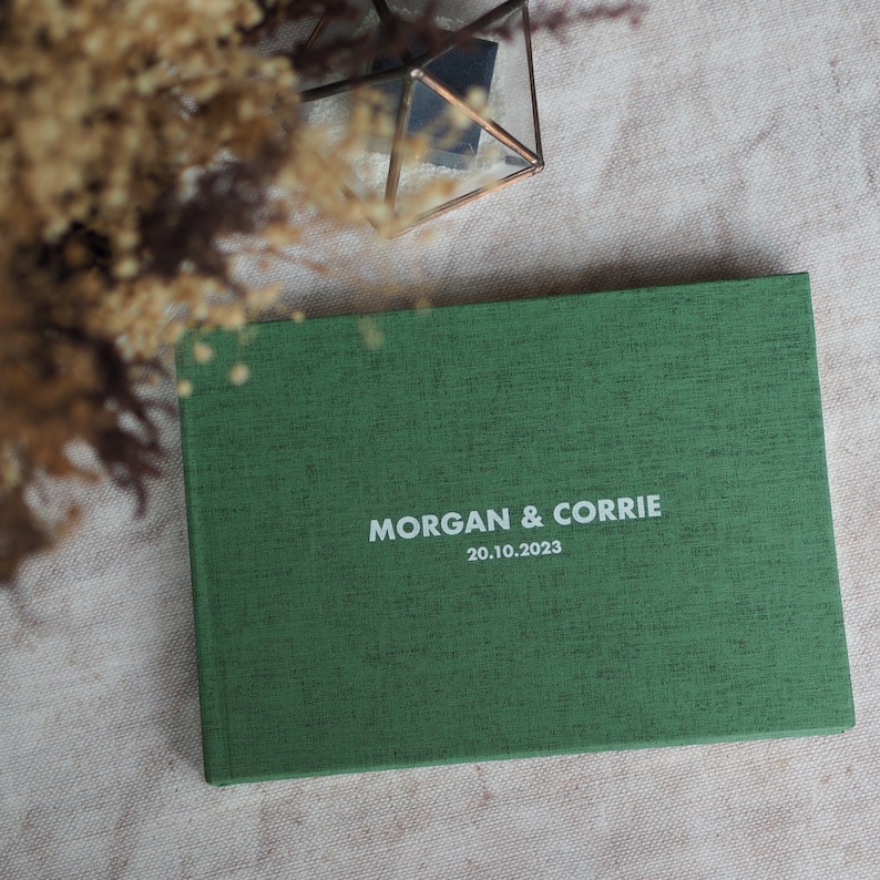 Puede incluir: Un libro de visitas de boda de textura de lino verde con el texto "MORGAN & CORRIE 20.10.2023" impreso en blanco.
