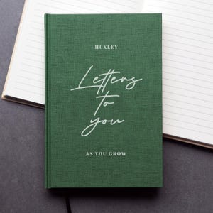 May include: A forest green hardback journal with a textured fabric finish. The cover features the white printed text HUXLEY, followed by the script text Letters To You, and the final line of text AS YOU GROW in a clean, sans-serif font.
