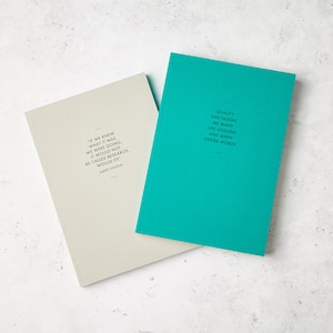 May include: Two notebooks with inspirational quotes. One is light gray with an Albert Einstein quote, the other is teal with a quote about life lessons. Both have black text and a minimalist design.