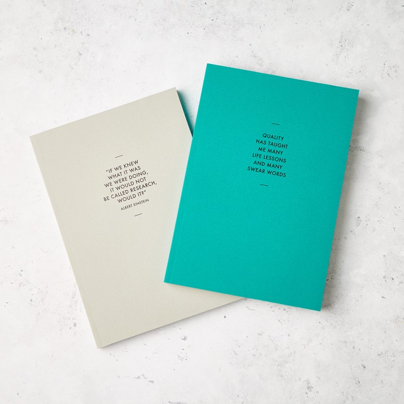 May include: Two notebooks with inspirational quotes. One is light gray with an Albert Einstein quote, the other is teal with a quote about life lessons. Both have black text and a minimalist design.