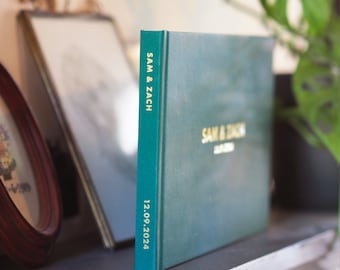 May include: A dark green hardcover photo album with gold foil lettering on the front and spine. The text on the front reads SAM & ZACH and 12.09.2024, while the spine features the text SAM & ZACH and 12.09.2024 in a vertical orientation.