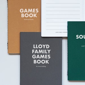 May include: Three different notebooks with the words "GAMES BOOK" on the front. The notebooks are brown, gray, and green. The brown notebook says "barthorpe family" on the front. The gray notebook says "LLOYD FAMILY GAMES BOOK for score tracking" on the front. The green notebook says "SOL sarah'" on the front.