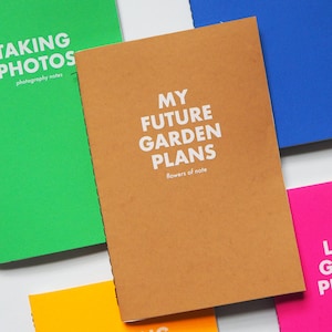 May include: Five different colored notebooks with white text on the covers. The notebooks are titled "Taking Photos", "My Future Garden Plans", "Camping Holidays", "Swimming", and "LGP".