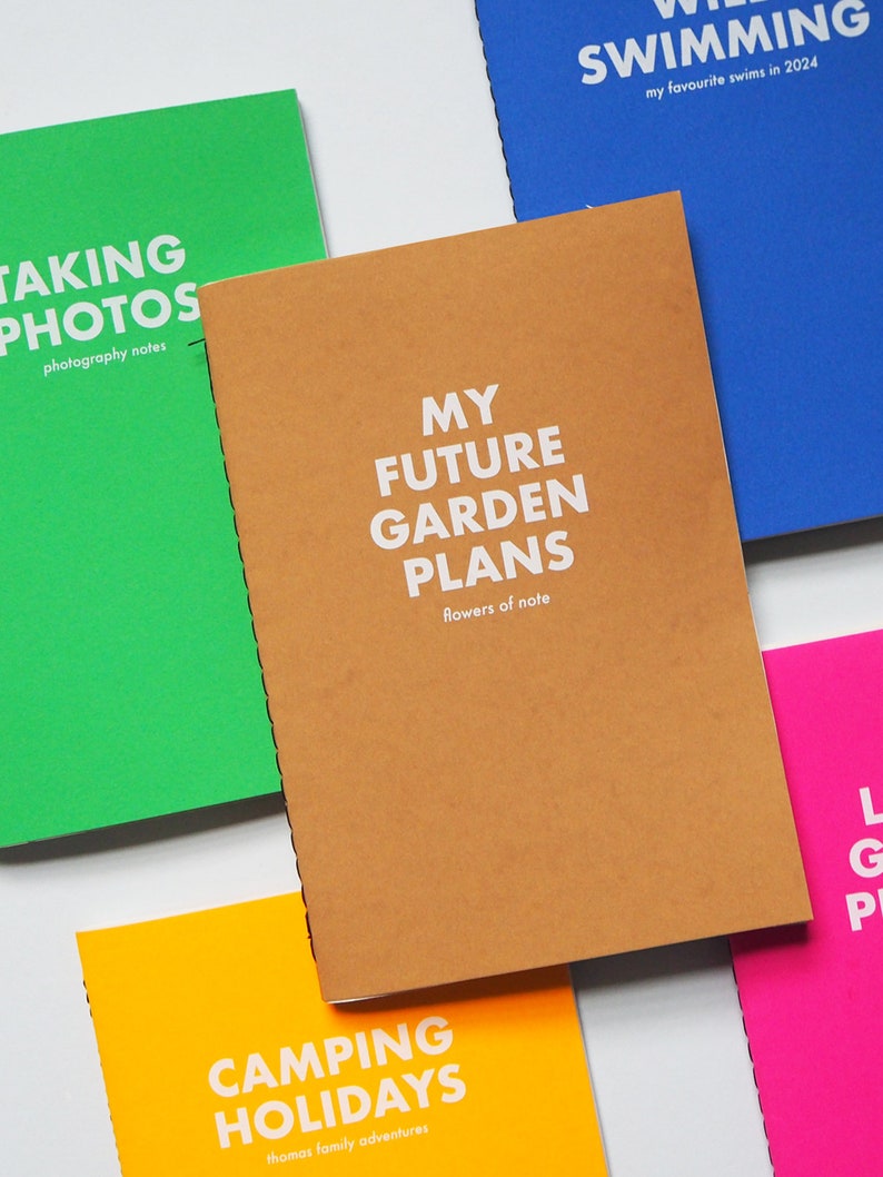 May include: Five different colored notebooks with white text on the covers. The notebooks are titled "Taking Photos", "My Future Garden Plans", "Camping Holidays", "Swimming", and "LGP".