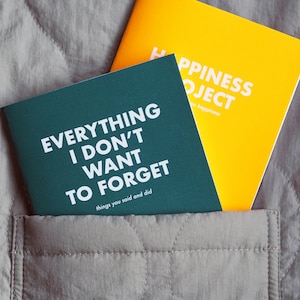 May include: Two small, hardcover journals with white text on colored covers. The green journal says "Everything I Don't Want To Forget, things you said and did". The yellow journal says "Happiness Project, on happiness".