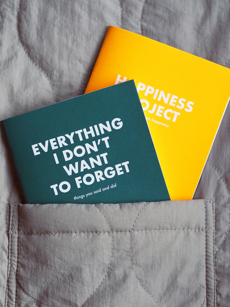 May include: Two small, hardcover journals with white text on colored covers. The green journal says "Everything I Don't Want To Forget, things you said and did". The yellow journal says "Happiness Project, on happiness".