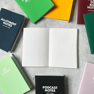 May include: A flat lay of various notebooks with different colored covers and titles. The notebooks are on a light gray surface. The titles include "Allotment Notes", "My Vows", "Podcast Notes", and "Book of Big Notes".