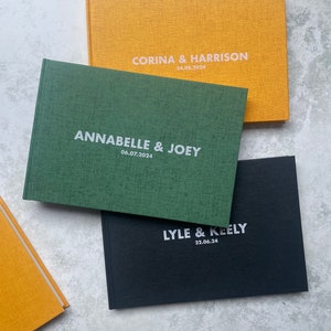 Puede incluir: Tres libros de visitas con cubiertas de diferentes colores. El libro superior es amarillo con el texto "Corina & Harrison 24.08.2024". El libro del medio es verde con el texto "Annabelle & Joey 06.07.2024". El libro inferior es negro con el texto "Lyle & Keely 22.06.24".