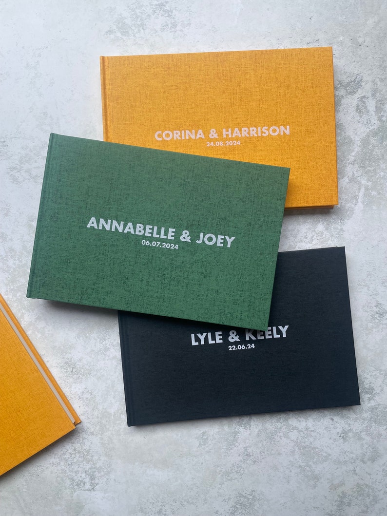 Puede incluir: Tres libros de visitas con cubiertas de diferentes colores. El libro superior es amarillo con el texto "Corina & Harrison 24.08.2024". El libro del medio es verde con el texto "Annabelle & Joey 06.07.2024". El libro inferior es negro con el texto "Lyle & Keely 22.06.24".