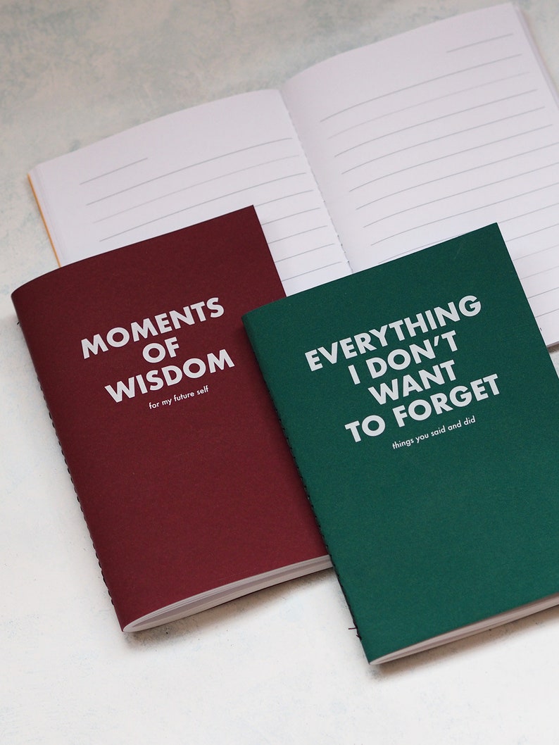 May include: Two small, lined notebooks with burgundy and green covers. The burgundy notebook has the text "Moments of Wisdom (for my future self)" printed on the front. The green notebook has the text "Everything I don't want to forget (things you said and did)" printed on the front.