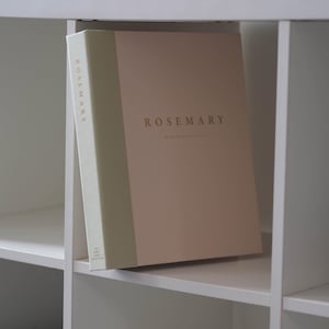 Può includere: Un libro dei ricordi con copertina rigida, dorso verde salvia chiaro e copertina rosa polvere. Il nome ROSEMARY è stampato in lamina d'oro sia sulla copertina che sul dorso. Sotto il nome, il testo riporta My Early School Years.