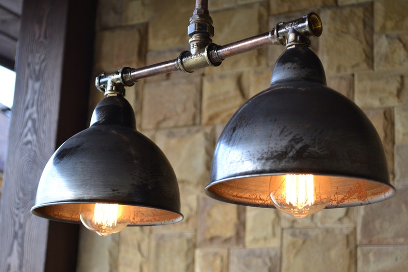 May include: Two black metal pendant lights with exposed copper pipe fixtures and Edison bulbs. The lights are hanging from a ceiling and are against a stone wall.