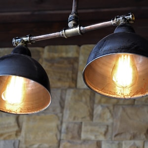 May include: Two black metal pendant lights with copper interiors and exposed Edison bulbs hanging from a copper pipe fixture.
