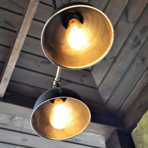 May include: Two black metal pendant lights with exposed bulbs hanging from a wooden ceiling. The lights have a gold finish and are illuminated.