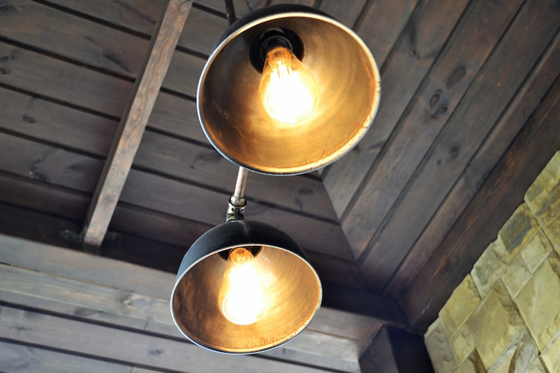 May include: Two black metal pendant lights with exposed bulbs hanging from a wooden ceiling. The lights have a gold finish and are illuminated.