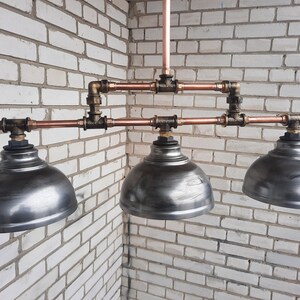 May include: A three-light industrial style pendant light fixture with copper pipes and three silver metal dome-shaped shades.