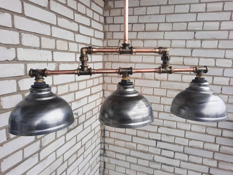 May include: A three-light industrial style pendant light fixture with copper pipes and three silver metal dome-shaped shades.