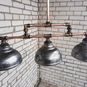 May include: A three-light industrial style pendant light fixture with copper pipes and metal shades. The shades are a brushed silver color.