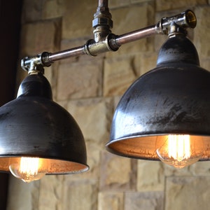 May include: Two black metal pendant lights with exposed copper pipe fixtures and Edison bulbs. The lights are hanging from a ceiling and are illuminated.