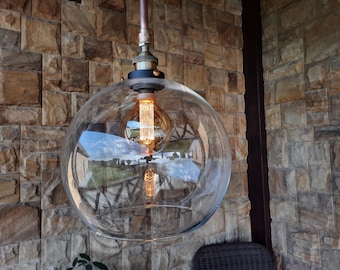 May include: A clear glass globe pendant light fixture with a copper and brass finish. The light fixture is hanging from a ceiling and has a single light bulb inside.