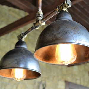 May include: Two industrial-style pendant lights with metal shades and exposed copper piping. The shades are a distressed silver color with a warm, golden interior. The lights are illuminated with Edison-style bulbs.