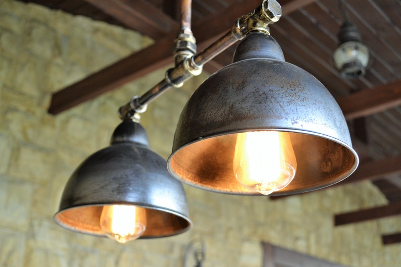 May include: Two industrial-style pendant lights with metal shades and exposed copper piping. The shades are a distressed silver color with a warm, golden interior. The lights are illuminated with Edison-style bulbs.