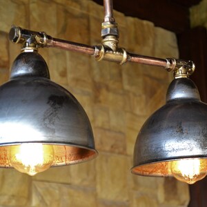 May include: Two industrial-style pendant lights with copper pipes and metal shades. The shades are a distressed silver color with a copper interior. The lights are hanging from a ceiling.