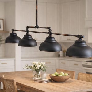 May include: A black, four-light kitchen island pendant light fixture with a bronze finish. The light features four dome-shaped shades and is suspended above a wooden dining table. The kitchen has white cabinets and a light-colored wooden table.