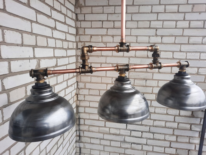 May include: A three-light copper pipe pendant light fixture with three silver metal dome-shaped shades.