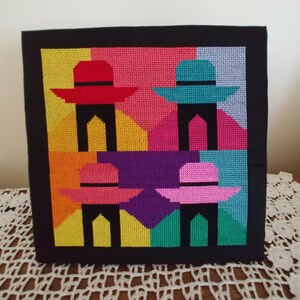 May include: A colorful cross-stitch design featuring four hats with black legs. The hats are red, blue, pink, and teal. The background is a patchwork of yellow, orange, pink, purple, green, and blue.