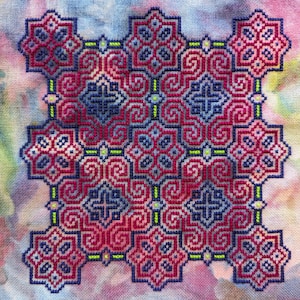 May include: A cross-stitch pattern with a geometric design featuring a repeating pattern of pink, blue, and green squares and swirls.