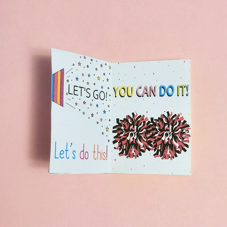 May include: A white card with a colorful design and the text "Let's go! You can do it! Let's do this!"  The card features a rainbow-colored megaphone with stars and two red and black pom-poms.