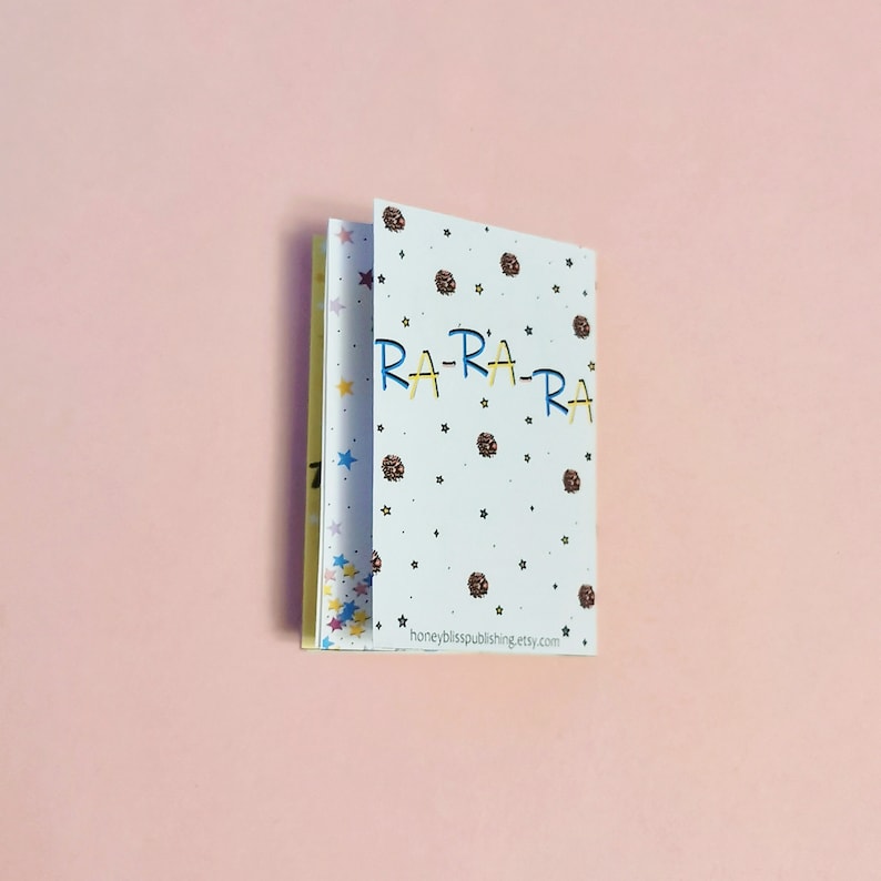 May include: A small, white booklet with a colorful star pattern on the cover. The text "RA-RA-RA" is written in blue and yellow letters on the front cover. The back cover has the text "honeybliss publishing.etsy.com".