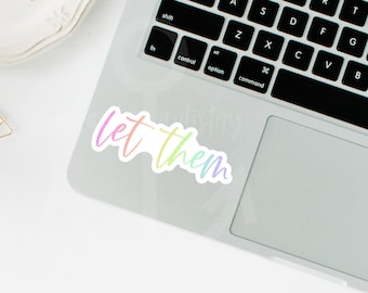 May include: A rainbow-colored sticker with the text "let them" on a silver laptop.